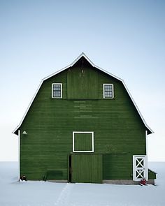 a large green barn with two windows in the snow