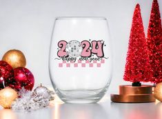 a wine glass sitting next to some christmas trees and ornaments on a table with the words happy new year printed on it