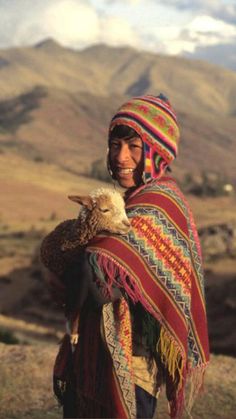 a woman with a bird in her arms on the side of a mountain range, wearing a colorful shawl and headdress