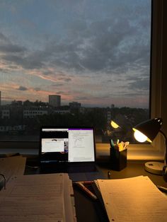 a laptop computer sitting on top of a desk next to an open book and lamp