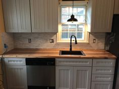 a kitchen with white cabinets and a black dishwasher under a window in the corner