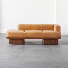 a tan leather couch sitting on top of a cement floor next to a white wall