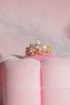 two gold rings sitting on top of a pink cushion next to a feathery pillow