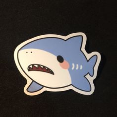 a blue and white shark sticker on a black surface with an angry look to it's face