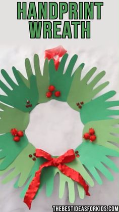 a handprint wreath made out of paper with red ribbon and holly berries on it