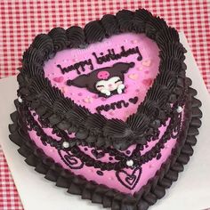 a heart shaped cake with black icing and pink frosting is on a table