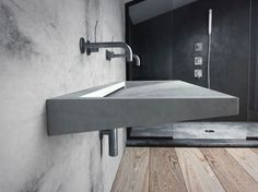 a concrete sink in a bathroom next to a wooden floor and shower head mounted on the wall