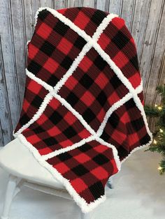 a red and black blanket sitting on top of a white chair next to a christmas tree