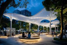 people are sitting on benches in the park at night with lit up canopy over them