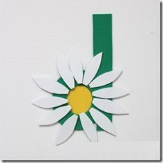 a white flower with yellow center sitting on top of a piece of green paper that is cut into the shape of a rectangle