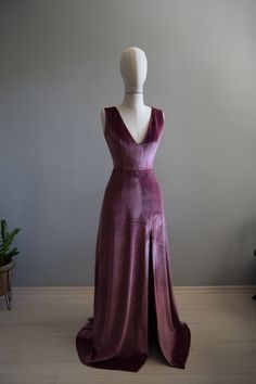 a mannequin wearing a long purple dress on top of a wooden floor next to a potted plant