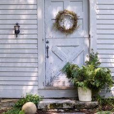 a white door with a wreath on it and two potted plants next to it