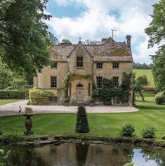 a large house sitting in the middle of a lush green field next to a pond