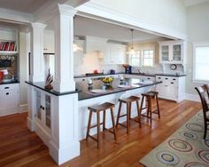 a kitchen with white cabinets and black counter tops, wooden flooring and an island in the middle