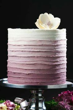 a white and pink frosted cake on a silver platter with flowers in the background