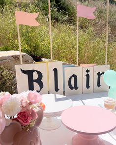 a table topped with cupcakes and pink flowers next to wooden blocks that spell out blarr