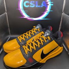 a pair of yellow and black shoes sitting on top of a display case in front of a logo