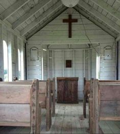 an empty church with wooden pews and a cross hanging from the ceiling above it