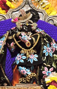 an elaborately decorated statue sitting on top of a purple and gold chair with flowers in the background