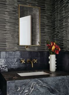 a bathroom sink sitting under a mirror next to a vase with flowers