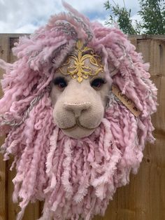 a close up of a stuffed animal wearing a pink and gold headdress on top of a wooden fence