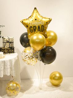 a bunch of black and gold balloons in front of a table with a star balloon