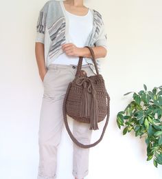 a woman holding a brown purse next to a potted plant on a white wall