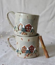 two mugs are stacked on top of each other with houses and trees painted on them