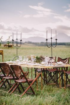 a table set up with chairs and candles in the middle of an open field for a dinner