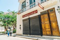 two people walking down the street in front of an old building with shuttered doors