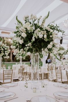 a vase filled with white flowers sitting on top of a table covered in plates and silverware