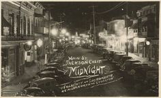 an old black and white photo of cars parked on the side of a street at night