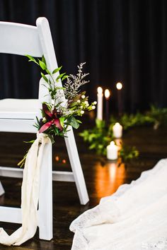 a white chair with flowers and greenery tied to it sitting on a wooden floor