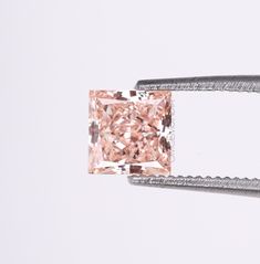 a fancy pink diamond is being held by a pair of tongs