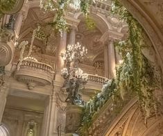 an ornate staircase with chandeliers and greenery on the ceiling in a building