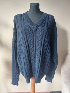 a blue cable knit sweater on a mannequin stand in front of a white wall