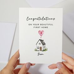 someone holding up a card that says congratulations on your beautiful first home with a house and heart