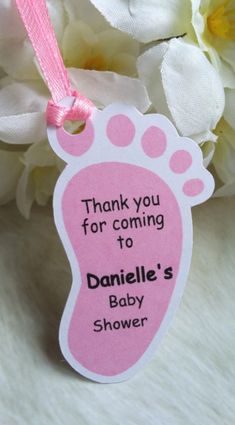 a pink baby foot ornament hanging from a ribbon with flowers in the background