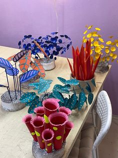 several vases with flowers on a table in front of purple walls and white chairs