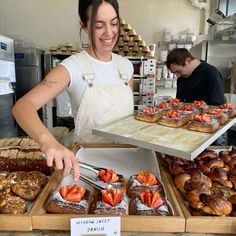 a woman is smiling as she puts strawberries on top of pastries in a bakery