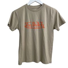 Von Dutch Unisex T-Shirt Size Youth L In Khaki With Orange Lettering, Nwot 100% Cotton Beige Crew Neck T-shirt With Logo Print, Beige Cotton T-shirt With Logo Print, Brown Cotton T-shirt With Logo Print, Brown Cotton Tops With Logo Print, Beige Graphic Tee With Logo Print, Brown Text Print T-shirt For Summer, Khaki Short Sleeve T-shirt With Letter Print, Khaki T-shirt With Letter Print, Short Sleeve, Summer Graphic Tee In Khaki