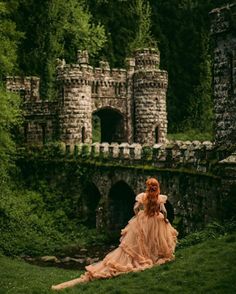 a woman in an orange dress is sitting on the grass near a stone bridge and castle