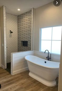 a large white bath tub sitting next to a window in a bathroom with wooden floors