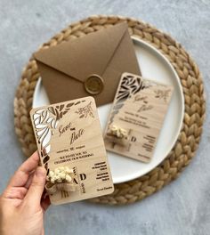 a person holding up a wooden wedding card on a plate with an envelope and flower