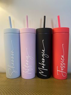 three different colored tumblers with straws in them sitting on a wooden table next to a lamp