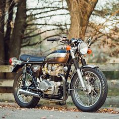 the motorcycle is parked on the side of the road in front of a wooden fence