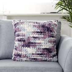 a purple and white pillow sitting on top of a gray couch next to a potted plant