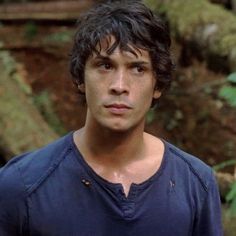 a young man standing in the woods looking at the camera with an intense look on his face