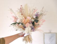 a hand holding a bouquet of flowers in front of a white wall with a painting on it