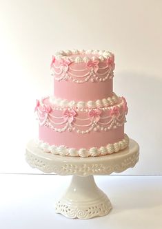 a three tiered cake with pink icing and flowers on top, sitting on a white pedestal